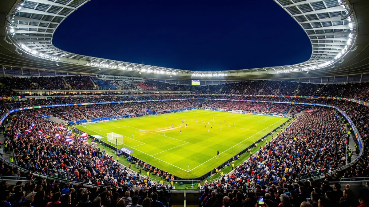 Estádio de futebol moderno iluminado durante jogo noturno com atmosfera vibrante
